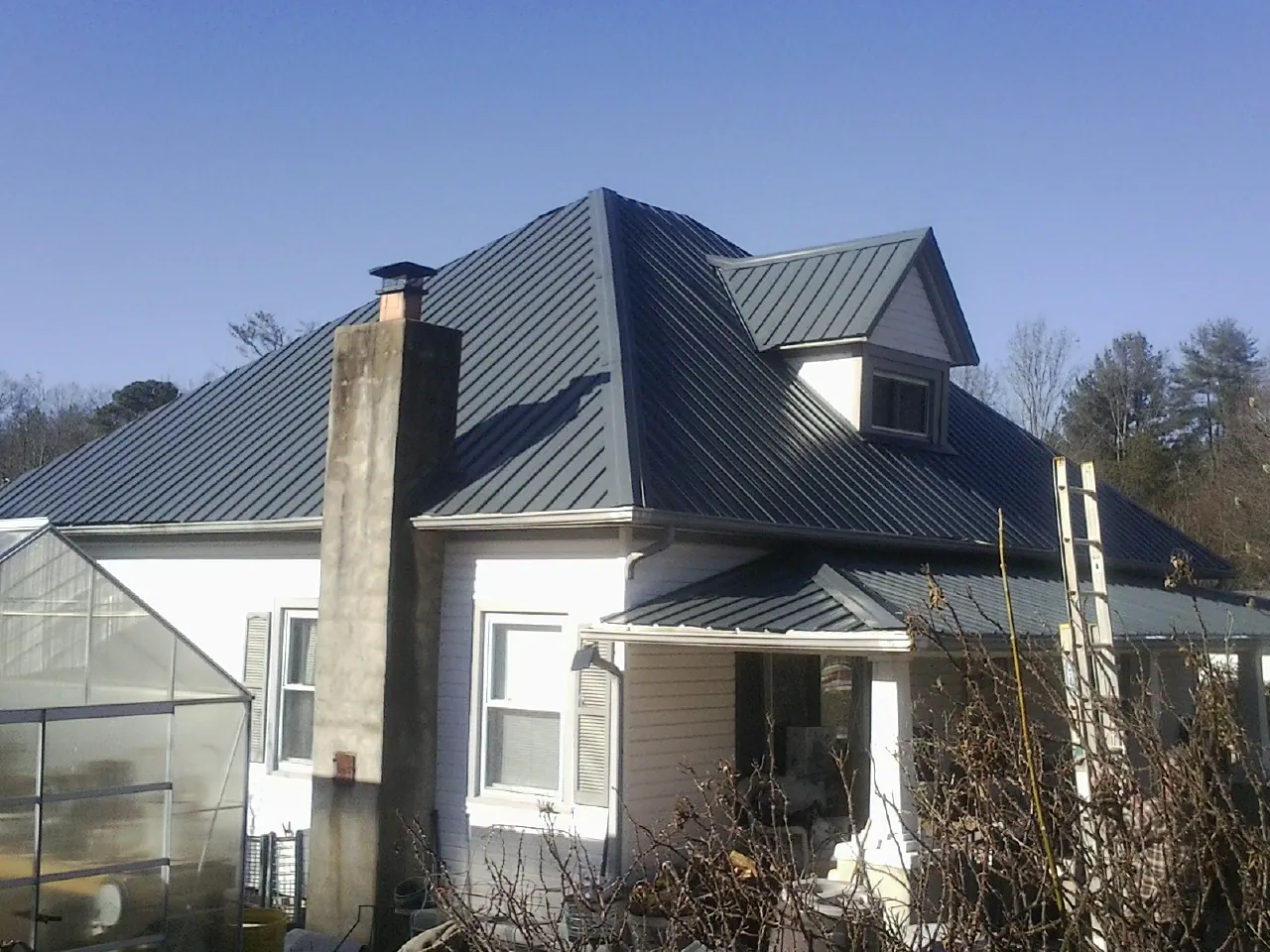 Dark blue standing seam metal roof on a white farmhouse with dormer — Slate & Tile Roof Repair by Roofing Brothers in Johnson City