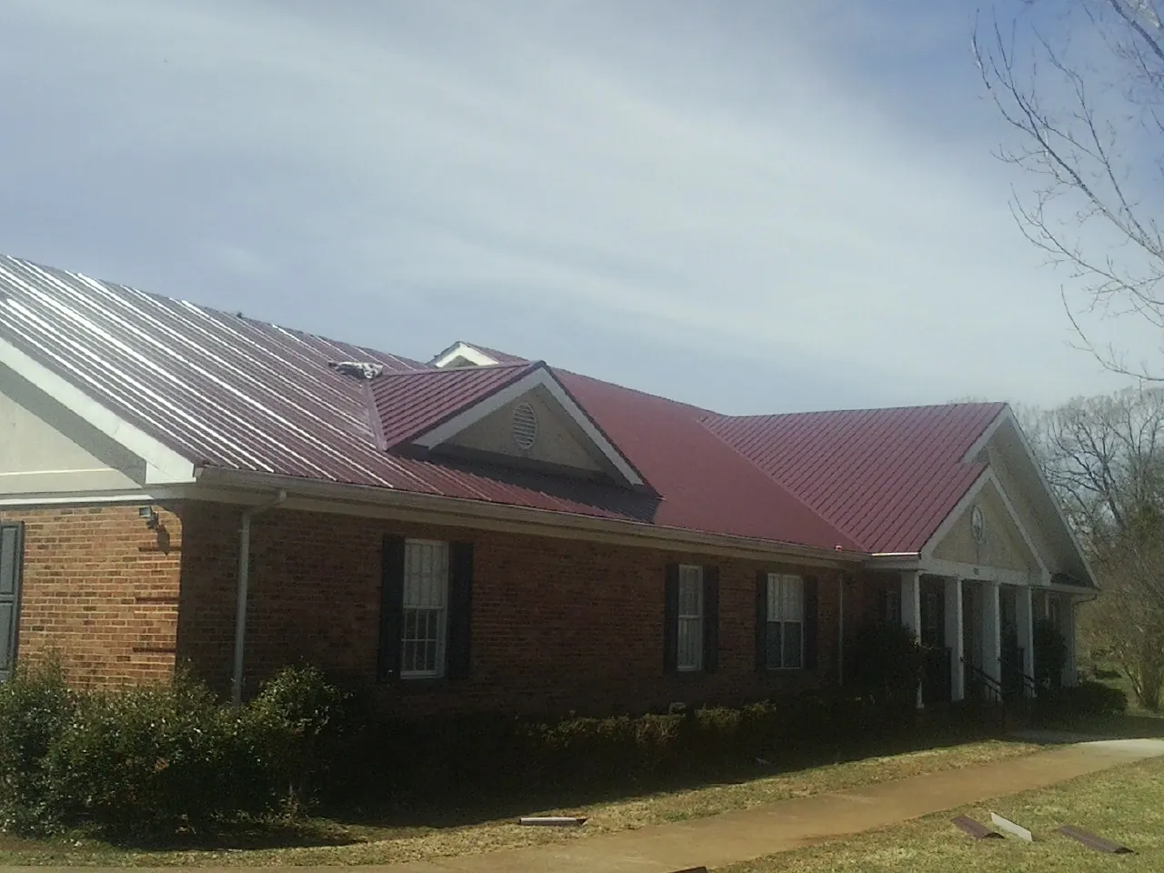 Red metal roof with gabled entries on a long brick building, from a Hail Damage Roof Repair job in Johnson City