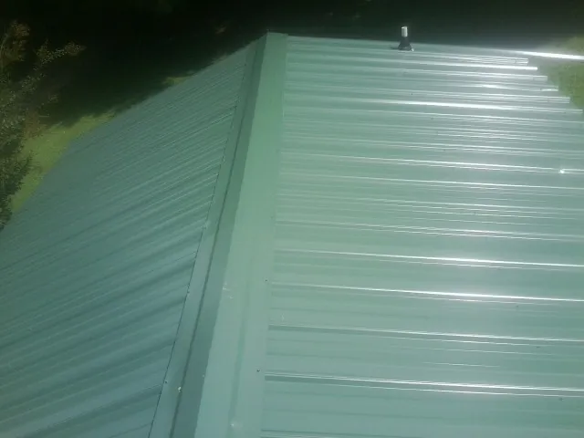 New green metal panels meeting at the ridge of a roof — Flat Roof Repair work by our crew in Johnson City